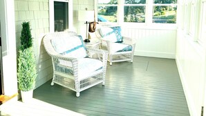 A covered porch with wicker furniture, a small plant, and a view of the outdoors. - New England, Coastal Beachside (DUXBURY)