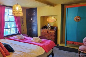 Une pièce comprenant un lit, une commode, une chaise, une fenêtre avec des rideaux et une porte ornée d’un miroir décoratif.