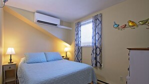 A bedroom with a bed, two bedside lamps, an air conditioning unit, a window with patterned curtains, and a wall decoration of birds. - Entire apartment, close to Hershey  (Palmyra)