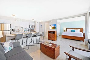 Quarto de hotel moderno com cozinha, área de refeições, sofá, mesa de centro de madeira e uma cama.