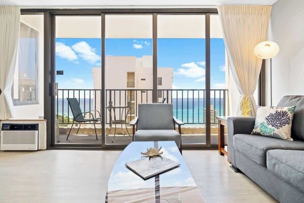 A room with a balcony, a sofa, a table, and a chair.