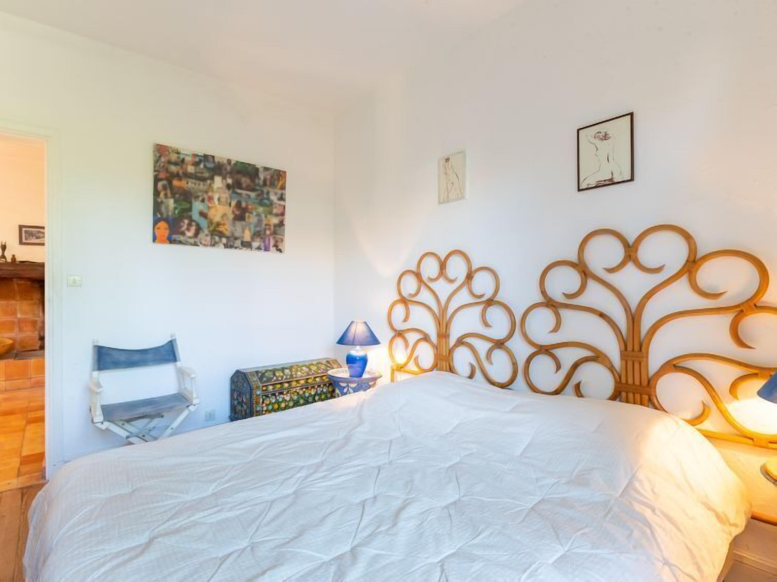 A bedroom with a bed, a chair, a lamp, and a wall with artwork.
