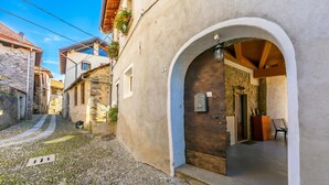 Une ruelle étroite pavée, bordée d’un bâtiment dont la façade est en pierre, avec une entrée en arc de cercle et une porte en bois.