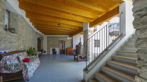 Un vaste espace de vie doté d’un plafond en bois, d’un escalier en pierre et d’un canapé confortable recouvert d’un tissu à motifs floraux.