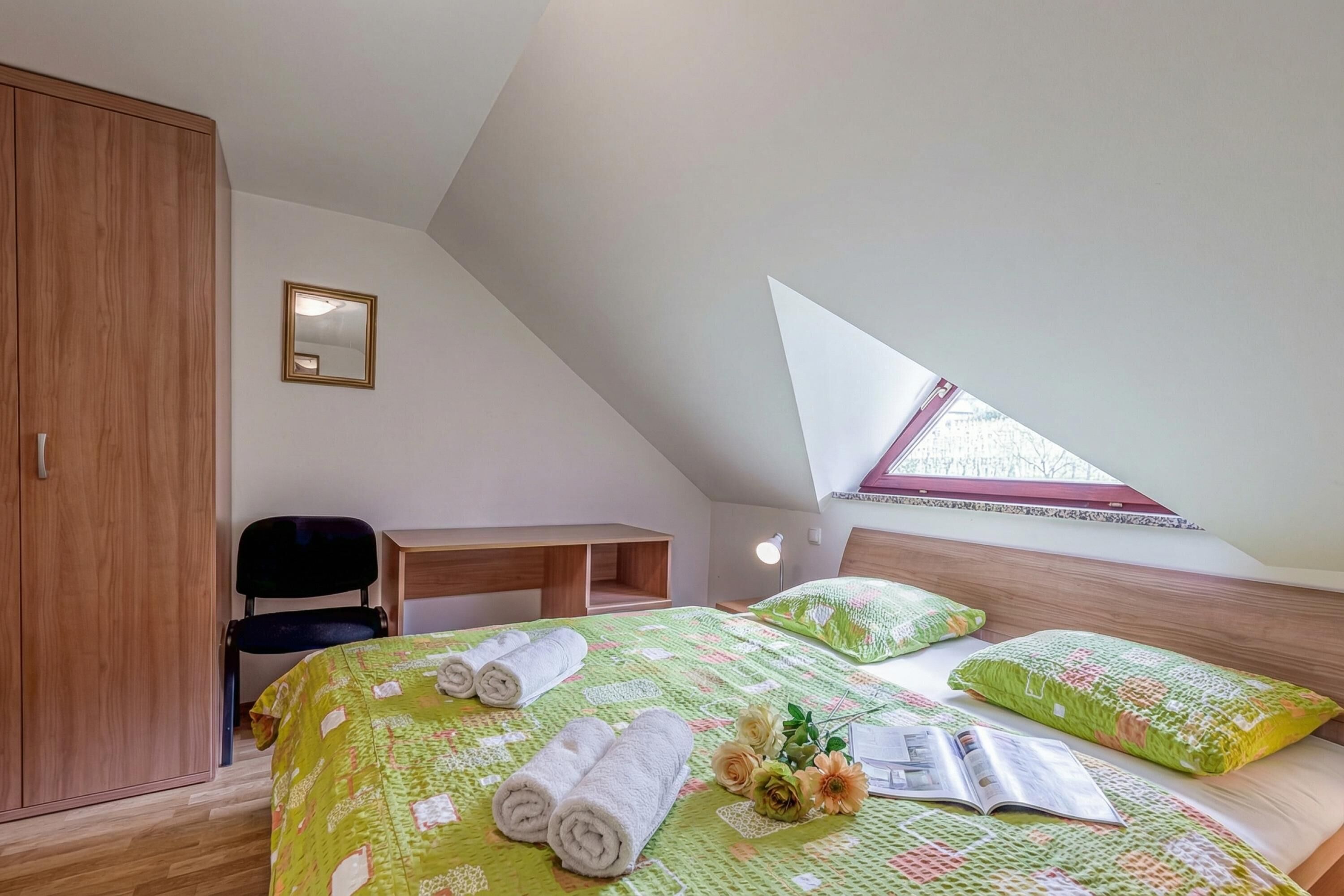 A bedroom with a bed, a desk, a chair, a wardrobe, and a window.