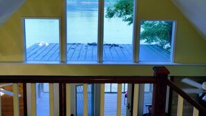 A room with a sloped ceiling and three windows overlooking a wooden deck and water. - Riverfront Retreat & Fisherman's Gold, on TN River (Savannah)