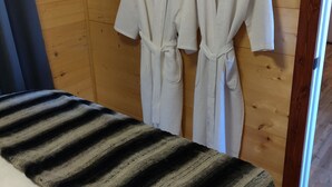 A bedroom with a wooden wall, two white robes hanging on hooks, a striped blanket on the bed, and a digital thermostat. - Riverfront Retreat & Fisherman's Gold, on TN River (Savannah)