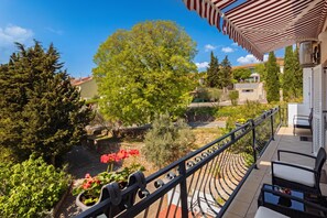 A balcony with a view of a garden, a tree, and a building in the background.