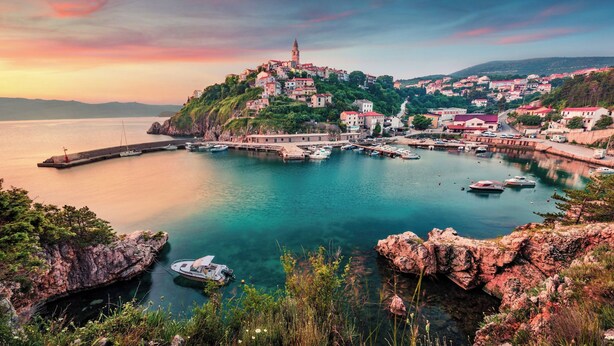 A coastal town with a prominent church on a hill, a marina with boats, and a rocky shoreline.