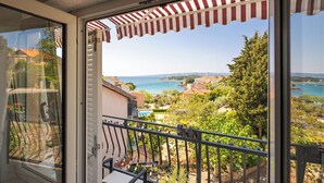A balcony with a view of a coastal town, a striped awning, and a clear sky.