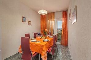 Uma sala de jantar com mesa posta para quatro pessoas, cadeiras, um candelabro e vista através de uma porta de vidro.