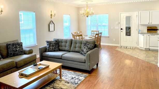 A spacious living room with a grey sofa, a wooden coffee table, and a chandelier.