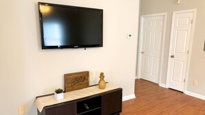 A living room with a flat-screen TV mounted on the wall, a dark wooden console table with a decorative item and a small plant, and a wooden floor.