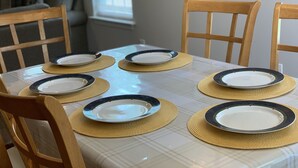 A dining table set with plates and placemats, surrounded by wooden chairs.