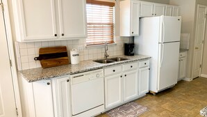A kitchen with white cabinets, a granite countertop, a coffee maker, and a refrigerator.