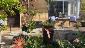 Une terrasse agrémentée de plantes en pot, d’une chaise en métal et d’une table avec un coussin bleu.