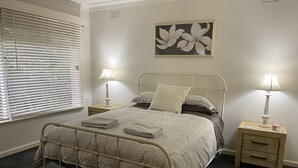 Un lit bien fait, avec une couvre-lit à motifs et des oreillers, deux tables de chevet avec des lampes, une œuvre d’art murale et une fenêtre avec des stores.