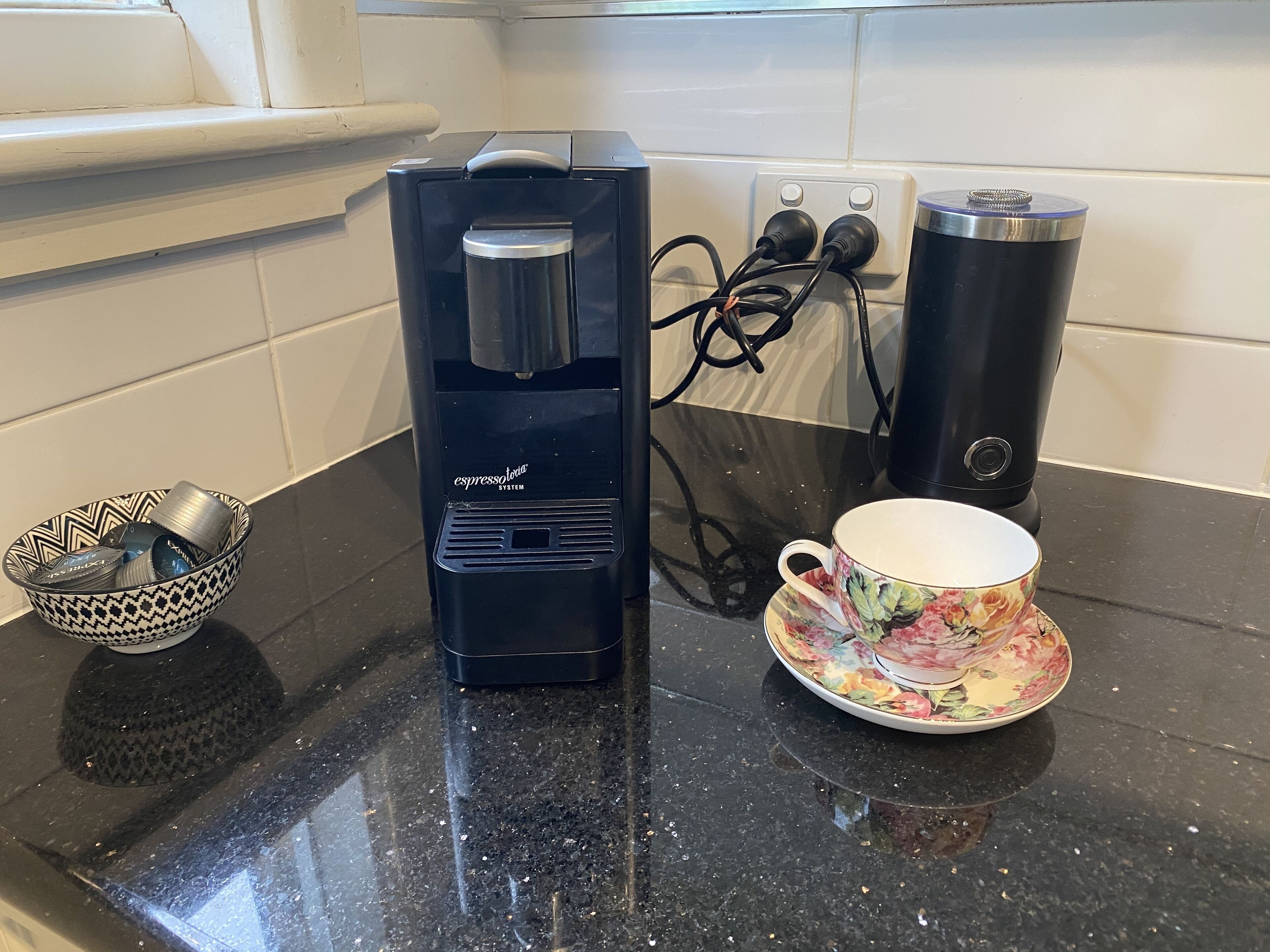 A coffee maker, a cup, and a bowl on a kitchen counter.