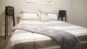 Un letto rifatto con cura, con copriletto e cuscini decorati, affiancato da due comodini neri.