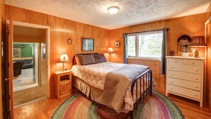 Ein Schlafzimmer mit einer holzgetäfelten Wand, einem Bett mit gemustertem Bettzeug, einem Schminktisch und einem Fenster mit Vorhängen.