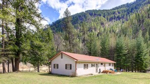Ein eingeschossiges Haus mit rotem Dach, umgeben von einer grünen Wiese und dichtem Wald.