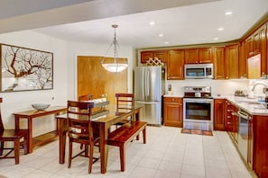 A modern kitchen with wooden cabinets, stainless steel appliances, and a dining area with a wooden table and chairs. - Amazing Location on Mtn w/Air Conditioning-100 yds to Trails-Heated Pool-Hot Tub-W/D in Unit-Grill (Steamboat Springs)