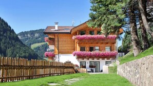 Una baita di legno con balconi decorati da fiori, con montagne sullo sfondo.
