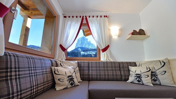 Una camera accogliente con divano, una finestra con tende, una mensola in legno e vista su una montagna.
