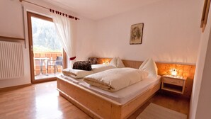 Un letto di legno con cuscini, un comodino con una lampada e vista sull'esterno attraverso una porta scorrevole.