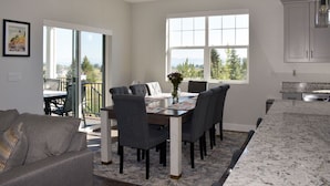 A modern kitchen with a large island, a dining area with a table and chairs, and a view of the outdoors through large windows. - Blue Lake Retreat - fully-landscaped home sits on 2nd tee of Bear Lake G.C. (Garden City)
