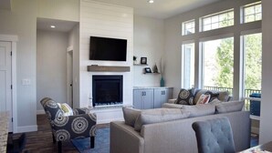 A modern living room with a fireplace, a sofa, a patterned armchair, and a television. - Blue Lake Retreat - fully-landscaped home sits on 2nd tee of Bear Lake G.C. (Garden City)