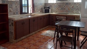 Uma cozinha com painel de azulejos, forno embutido, mesa de jantar com cadeiras e luminárias pendentes.