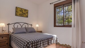 Quarto com cama, duas mesas de cabeceira com luminárias, uma janela com cortinas e uma obra de arte na parede.