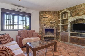 A living room with a stone fireplace, a television, and a sofa. - Vacation Home Casa del Patio with Wi-Fi, A/C & Terraces (Barbate)