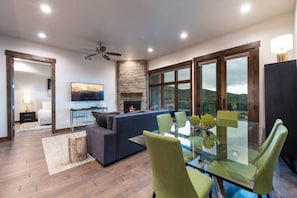A modern living room with a glass dining table, green chairs, a fireplace, and a large window offering a view of the outdoors. - Blackstone Lofts 2B (Park City)