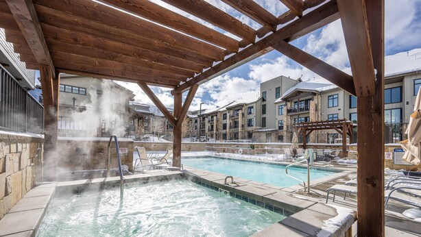Ein Whirlpoolbereich mit einer hölzernen Pergola darüber, umgeben von Steinmauern und einem Pool.