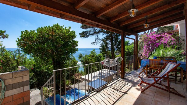 Un'area esterna coperta con piscina, posti a sedere e vista sul mare.