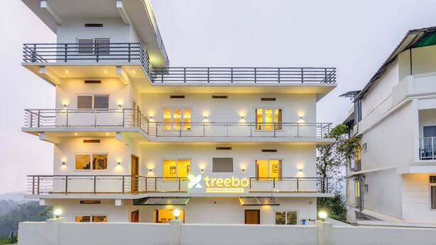 Ein mehrstöckiges Gebäude mit Balkonen, einem Schild mit der Aufschrift "treebo" und einer gut beleuchteten Fassade.
