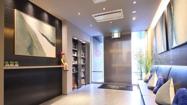 A reception area with a reception desk, a sofa with cushions, a large abstract painting, a bookshelf, and a wall-mounted air conditioning unit. - Dynasty Hotel & Resort Osaka (Osaka)