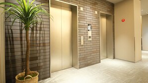A modern elevator with a digital display, a potted plant, and a wall with a brick pattern. - Dynasty Hotel & Resort Osaka (Osaka)
