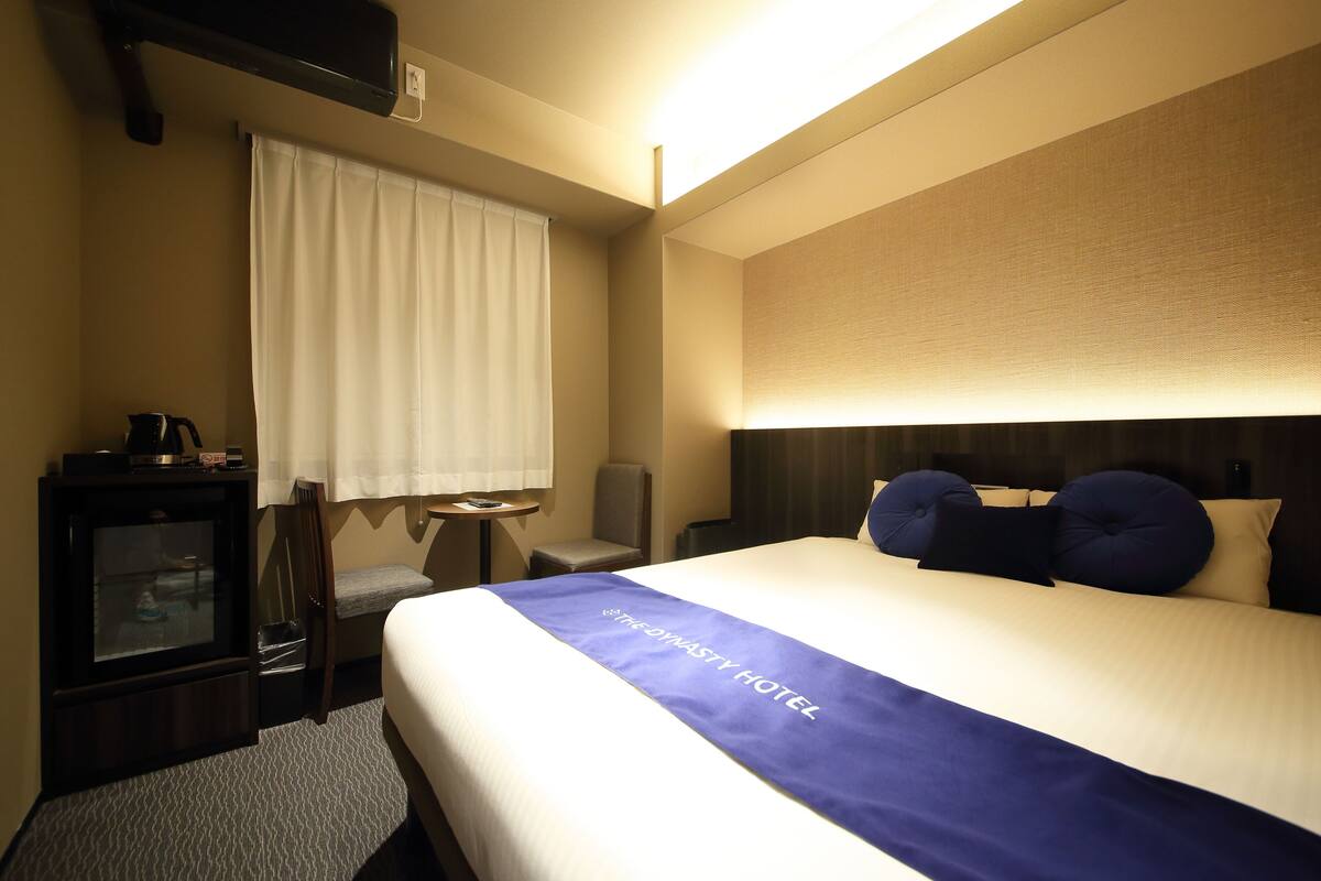 Una habitación de hotel con cama, escritorio, silla, mesita y ventana con cortinas.