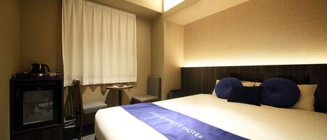 Une chambre d’hôtel avec un lit, un bureau, une chaise, une petite table et une fenêtre avec des rideaux.