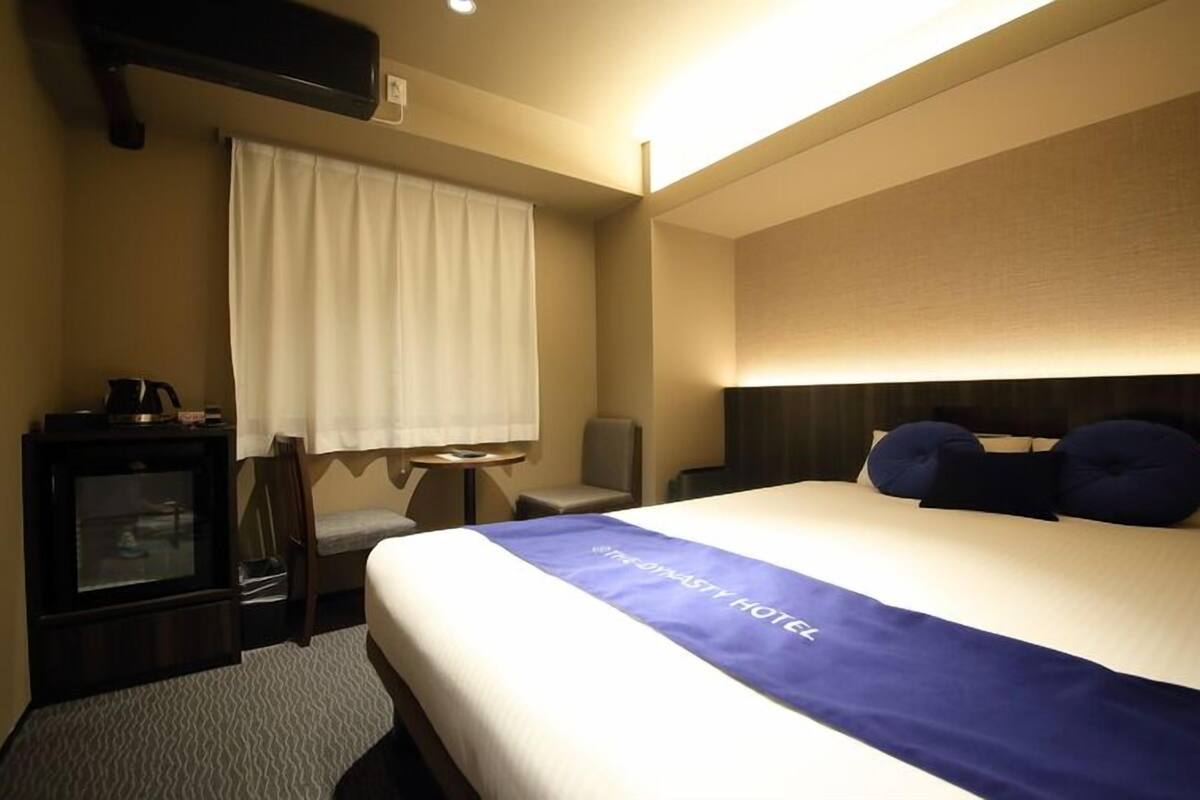 Una habitación de hotel con cama, escritorio, silla, televisión y ventana con cortinas.