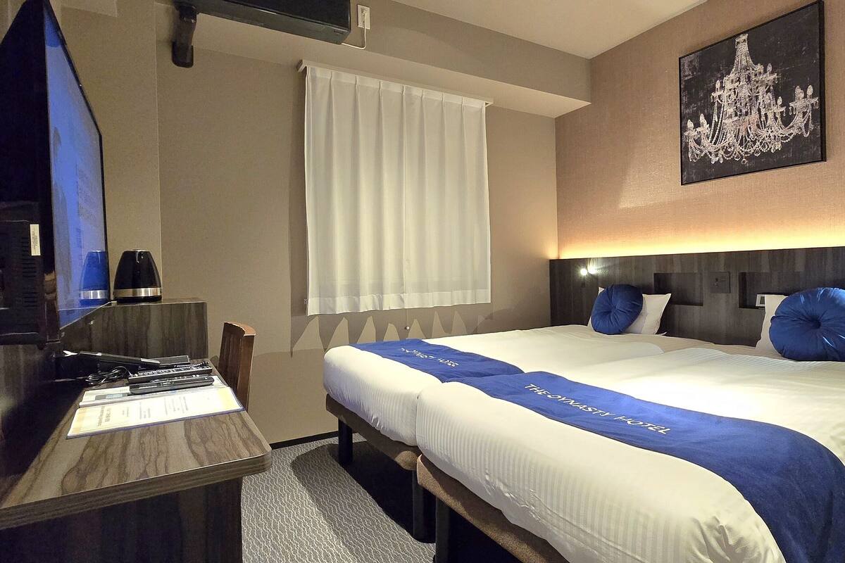 Habitación de hotel con cama, escritorio, silla, televisor y candelabro.