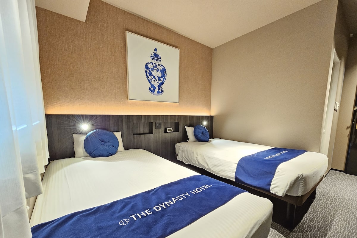 Habitación de hotel con dos camas, cada una con cubrecama azul y almohada. Se observa una obra de arte enmarcada sobre las camas, un cabecero con iluminación integrada y piso alfombrado.