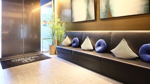 A modern lobby with a reception desk, a waiting area with a sofa and decorative pillows, and abstract wall art. - Dynasty Hotel & Resort Osaka (Osaka)