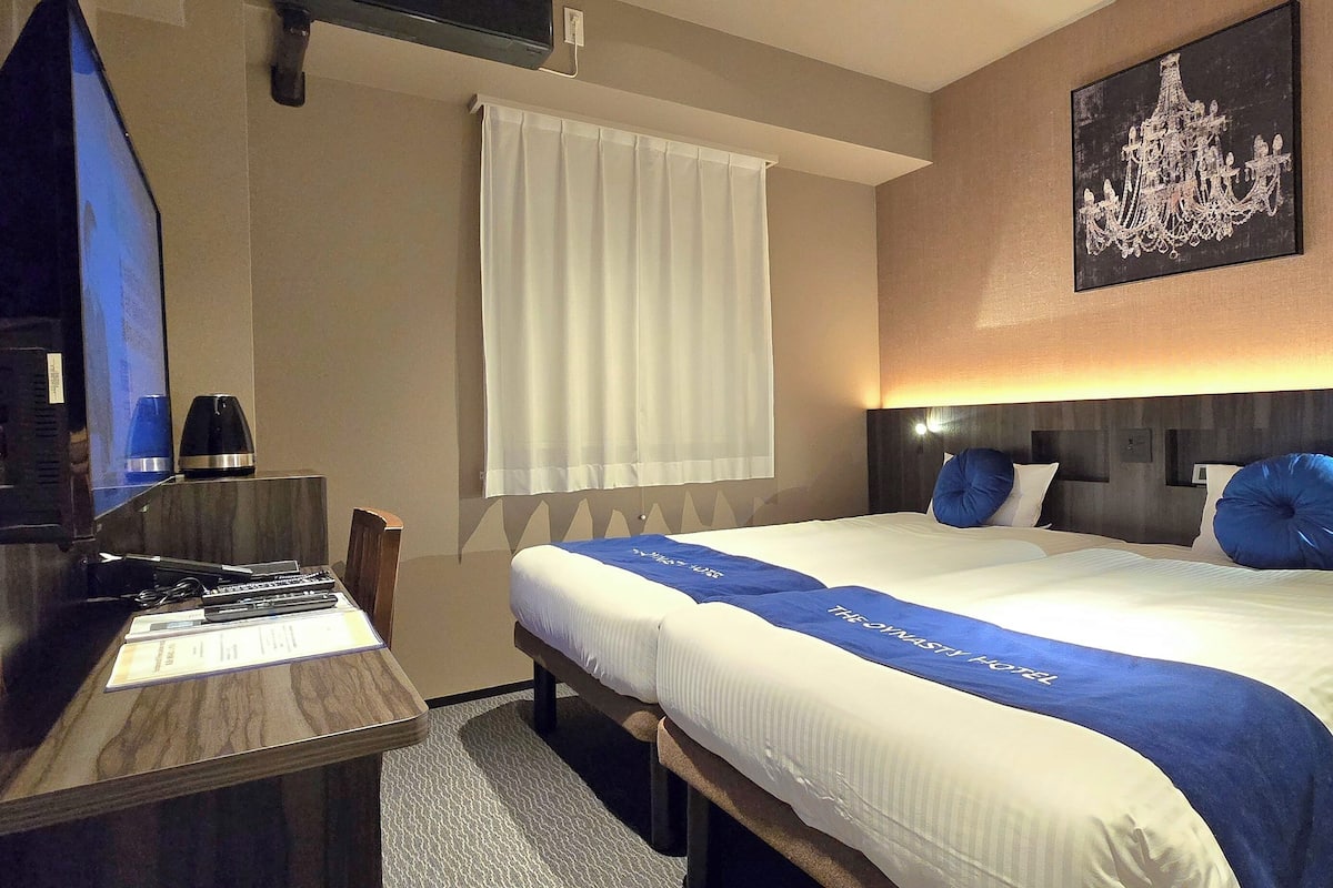 Habitación de hotel con cama, escritorio con computadora, silla, ventana con cortinas y un candelabro en la pared.