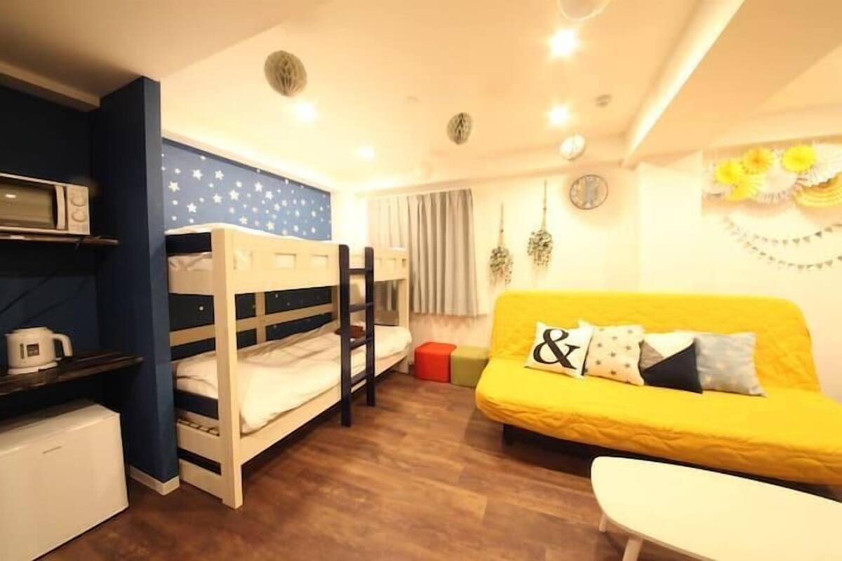 A compact room with bunk beds, a yellow sofa, a small table, and a microwave.