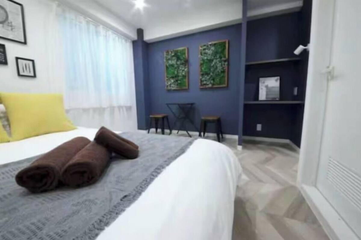 A hotel room with a bed, a desk, two chairs, and artwork on the wall.