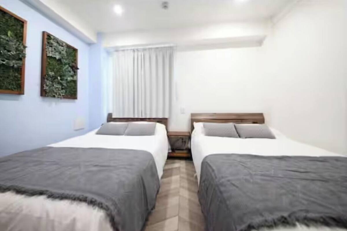 A hotel room with two single beds, a window with curtains, a wall-mounted plant, and a wooden headboard.